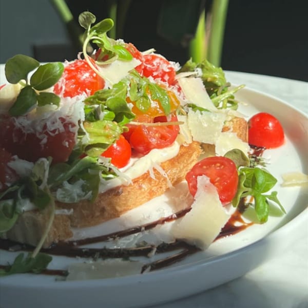 Toasted bread topped with cherry tomatoes, fresh greens, shaved cheese, and a balsamic glaze.