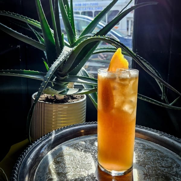 A tall glass of iced orange cocktail with an orange slice, on a silver tray.