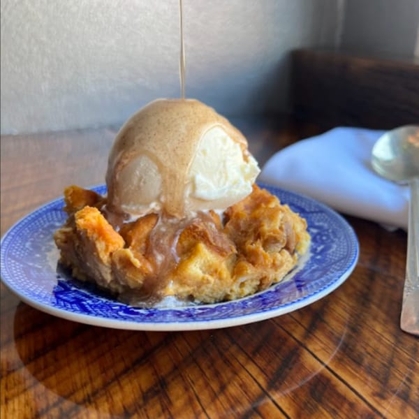 Bread pudding with a scoop of vanilla ice cream and caramel drizzle on a blue and white plate.