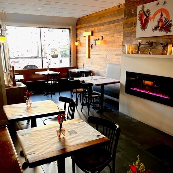 The Tasty's dining room with wooden tables, black chairs, a fireplace, and a large window.