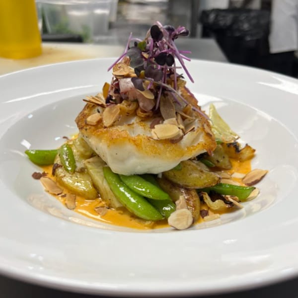 Pan-seared fish with snap peas, potatoes, almonds, and purple microgreens on a white plate.