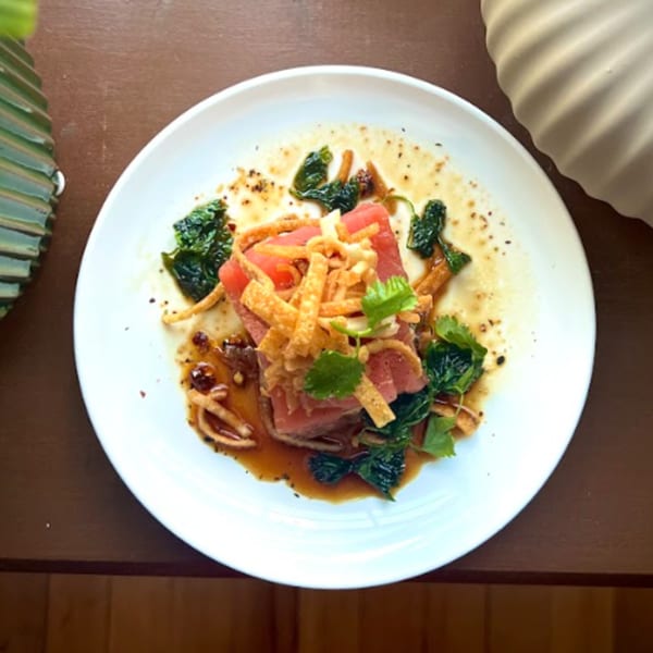 Seared tuna with crispy wontons, greens, and sauce, served on a white plate at The Tasty.
