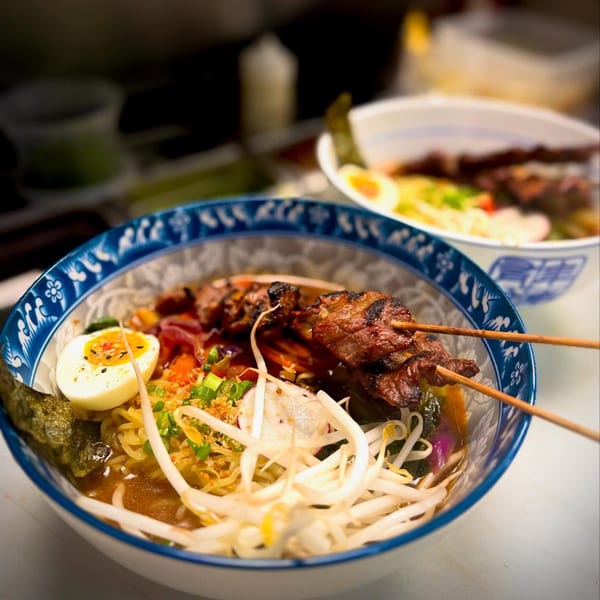 Two bowls of ramen with grilled meat skewers, soft-boiled egg, bean sprouts, and nori.