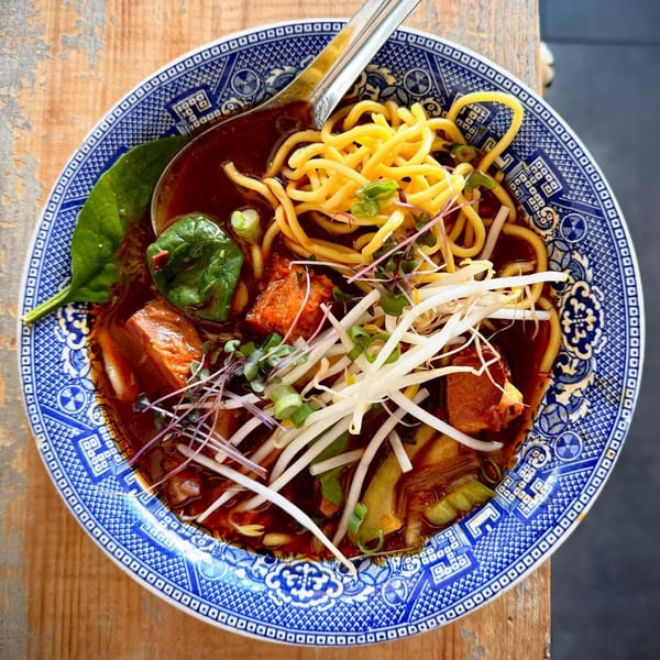 A blue and white bowl of ramen with noodles, pork belly, spinach, and bean sprouts.