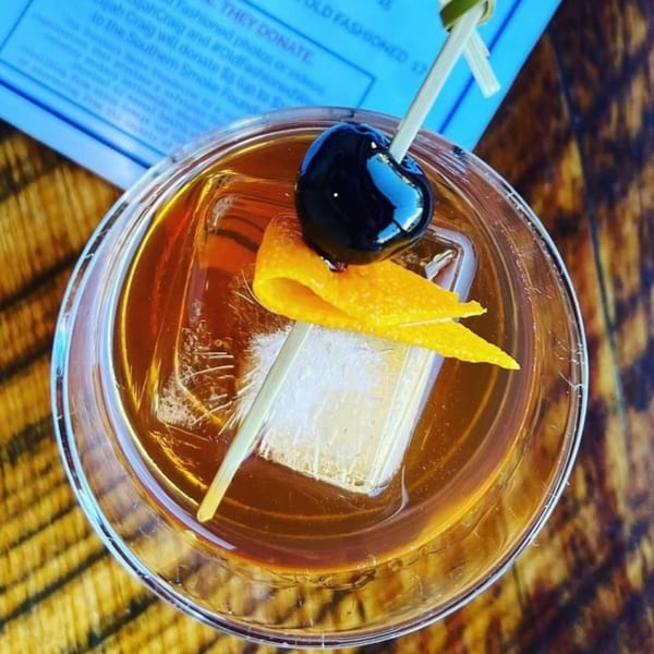 Overhead view of an Old Fashioned cocktail with a large ice cube, orange peel, and cherry.